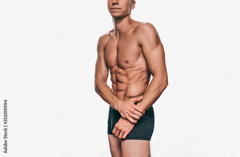 Attractive Caucasian male model in black underwear showing his sexy body on a white background. Portrait of sporty healthy shitless man with sexy abdomen and biceps posing over white wall. Health