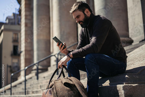 Attractive bearded businessman using mobile smartphone outside. Blurred background