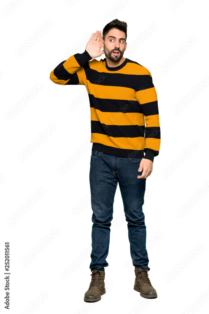 Full-length shot of Handsome man with striped sweater listening to something by putting hand on the ear on isolated white background Full-length shot of Handsome man with striped sweater listening to something by putting hand on the ear on isolated white background