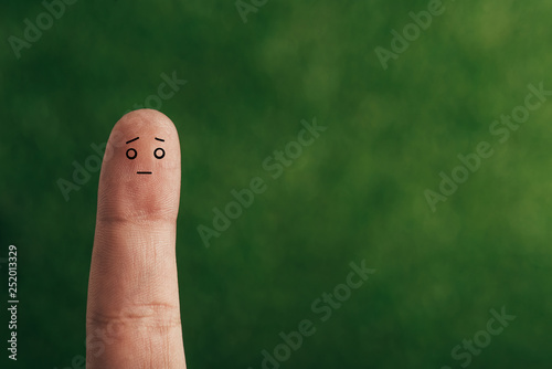 cropped view of one finger with confused face on green