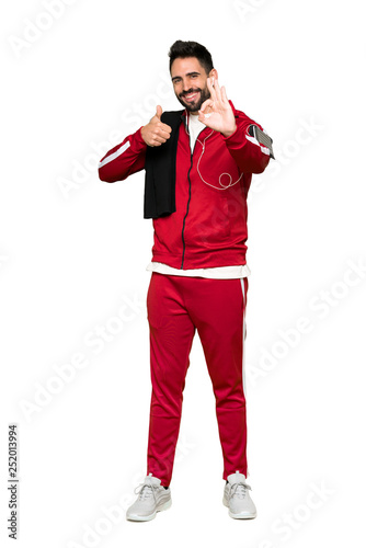 Full-length shot of Handsome sportman showing ok sign with and giving a thumb up gesture on isolated white background © luismolinero