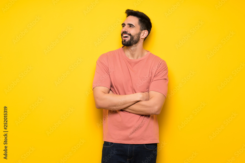 Handsome man over yellow wall keeping the arms crossed while smiling