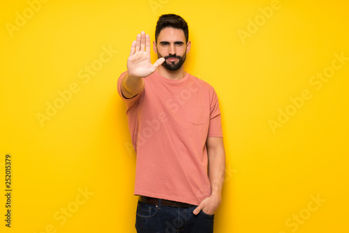 Handsome man over yellow wall making stop gesture denying a situation that thinks wrong