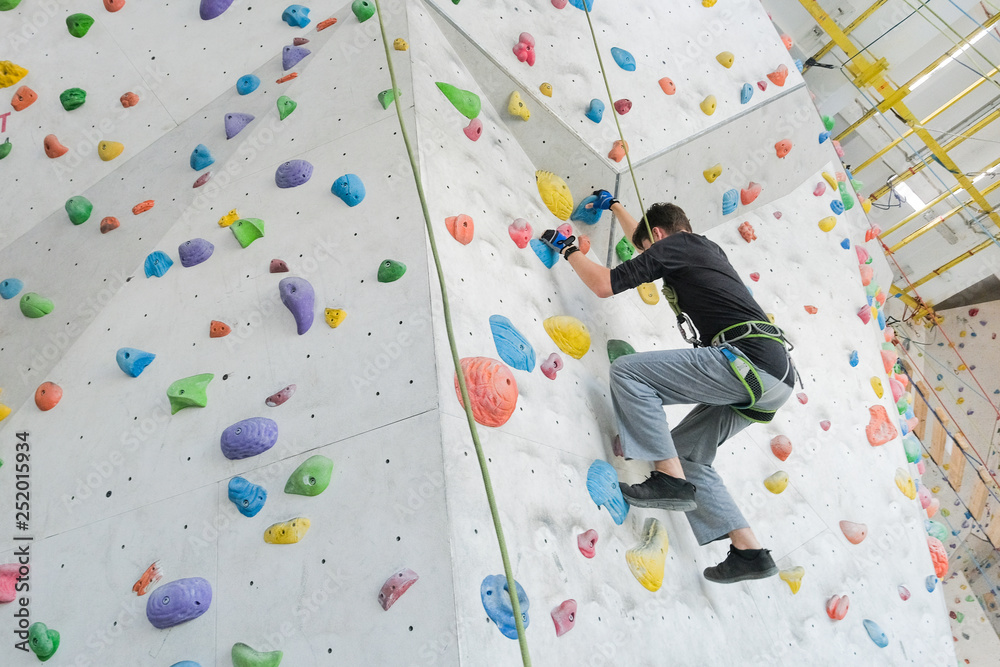 Sportsmen climbs boulder in a gym. A successful man climbing on climbing wall.