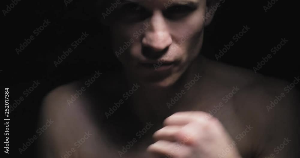 Muscular young man shows the different movements and strikes in the studio on a dark background Muscular young man shows the different movements and strikes in the studio on a dark background