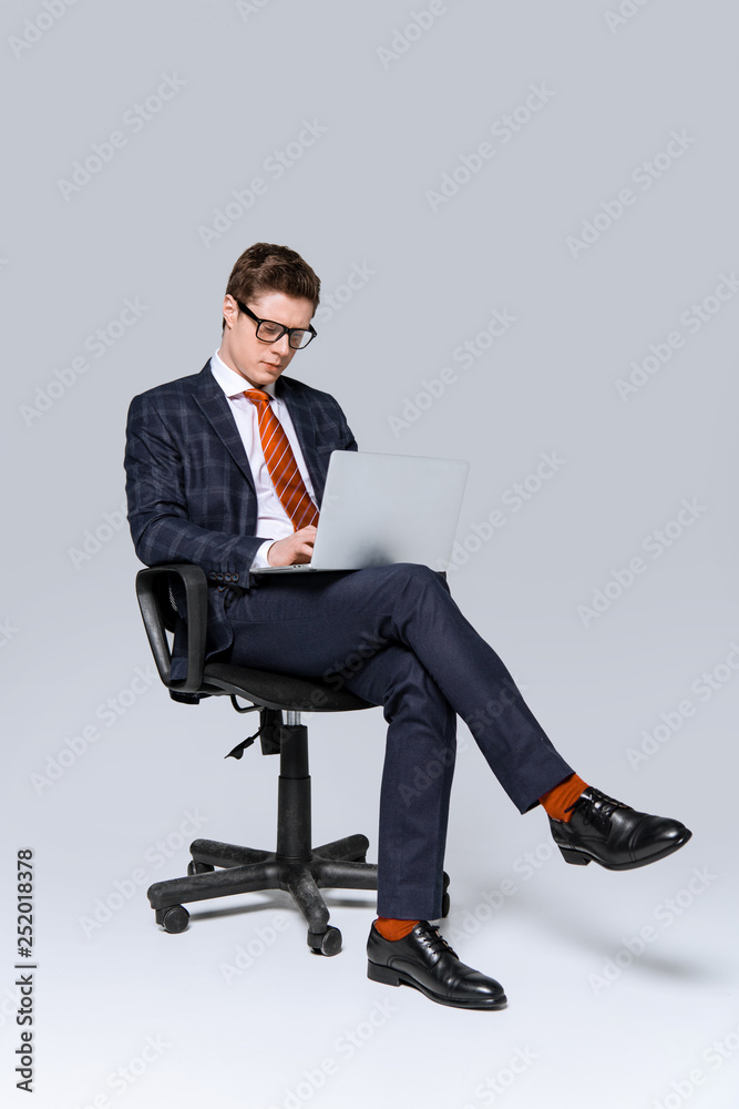 businessman sitting on chair and working on laptop on grey businessman sitting on chair and working on laptop on grey