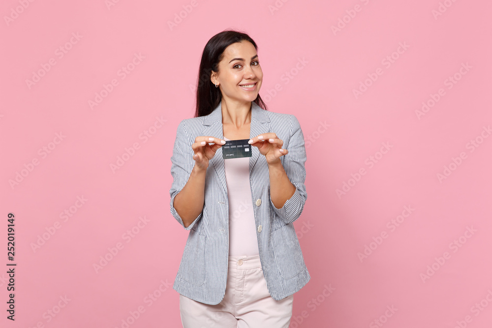 Portrait of smiling pretty young woman in striped jacket holding credit bank card isolated on pink pastel wall background in studio. People sincere emotions, lifestyle concept. Mock up copy space. Portrait of smiling pretty young woman in striped jacket holding credit bank card isolated on pink pastel wall background in studio. People sincere emotions, lifestyle concept. Mock up copy space.