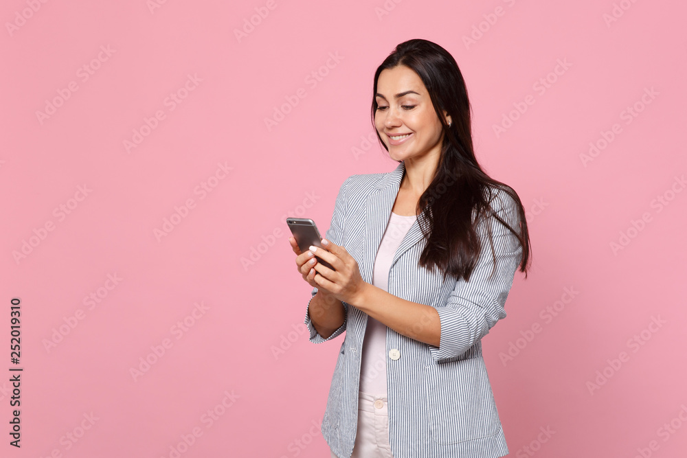 Portrait of smiling young woman in striped jacket using mobile phone, typing sms message isolated on pink pastel background in studio. People sincere emotions, lifestyle concept. Mock up copy space. Portrait of smiling young woman in striped jacket using mobile phone, typing sms message isolated on pink pastel background in studio. People sincere emotions, lifestyle concept. Mock up copy space.