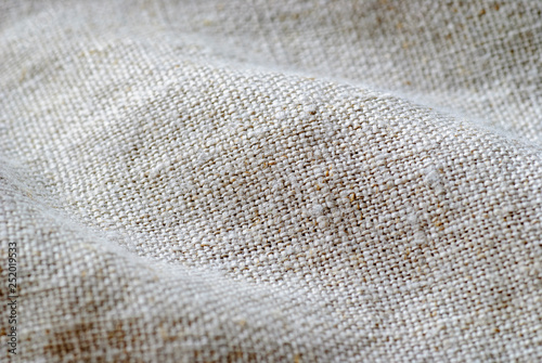 Texture if natural linen fabric draped in waves in a full frame background with shallow dof and copy space