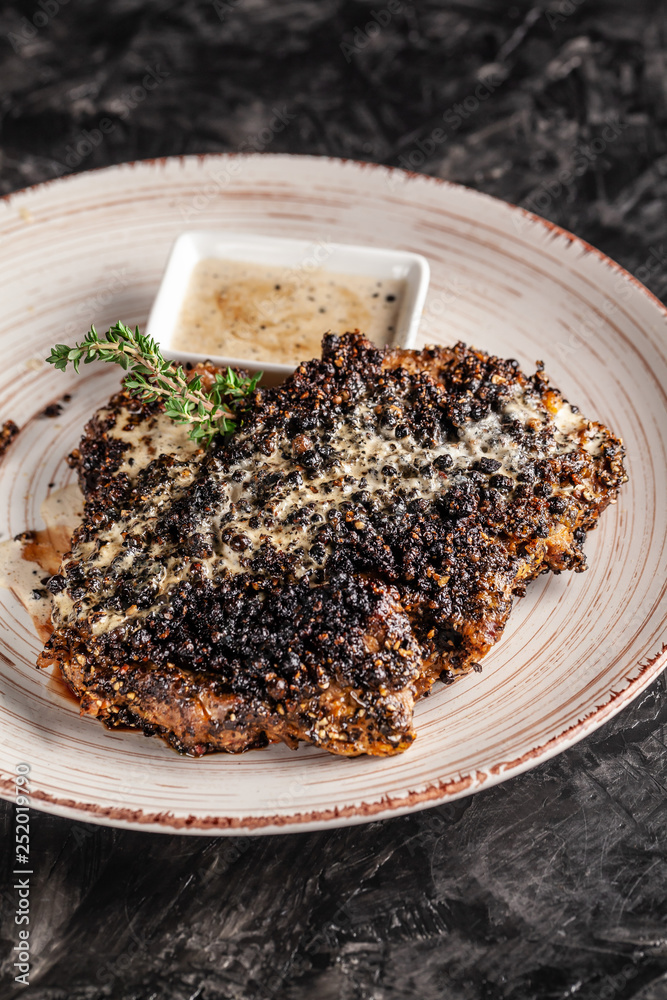 The concept of American cuisine. Fried, juicy pork steak in black pepper with thyme and white cheese sauce on a white ceramic dish. Serving dishes in the restaurant. copy space The concept of American cuisine. Fried, juicy pork steak in black pepper with thyme and white cheese sauce on a white ceramic dish. Serving dishes in the restaurant. copy space