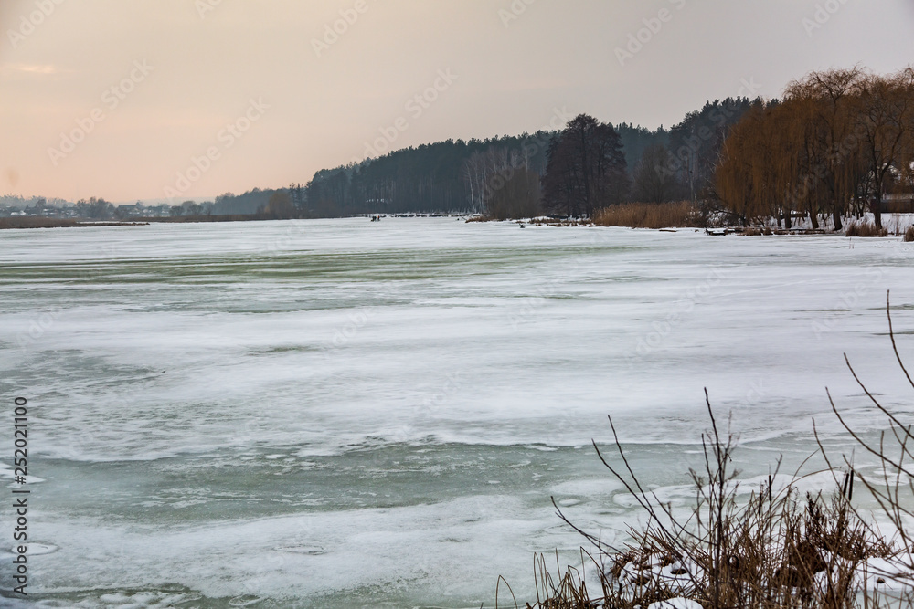 Fototapeta premium icy frozen lake in the background of the forest in the sunset rays of the sun