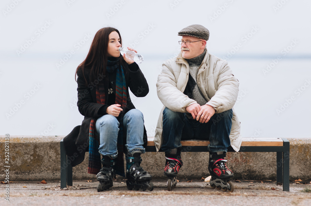Father and daughter on roller skates sit on a bench. A girl on rollers  drinks water from a bottle. Sport and water. Active old people in  retirement. Stock Photo | Adobe Stock