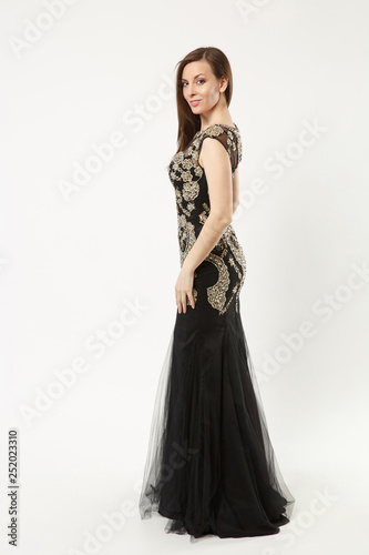Full length photo fashion model woman wearing elegant evening dress black gown posing isolated on white wall background studio portrait. Brunette long hair girl. Mock up copy space. Side profile view.