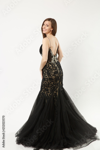 Full length photo of fashion model woman wearing elegant evening dress black gown posing isolated on white wall background studio portrait. Brunette long hair girl. Mock up copy space. Back rear view.