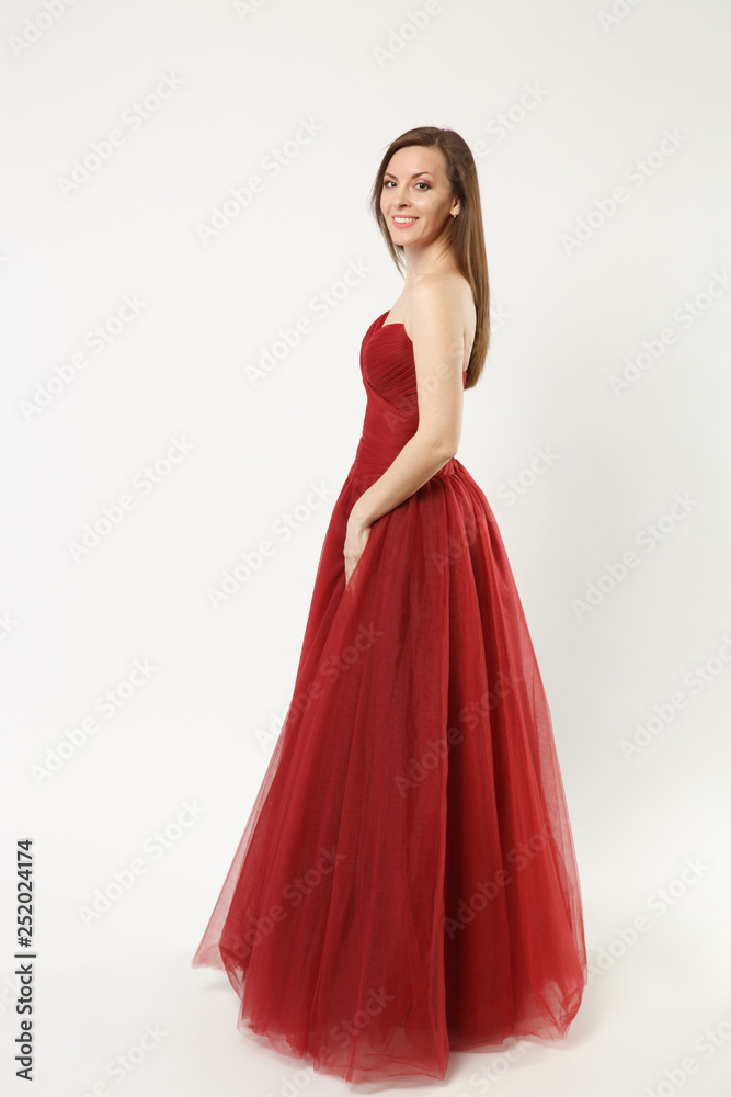 Full length photo fashion model woman wearing elegant evening dress red gown posing isolated on white wall background studio portrait. Brunette long hair girl. Mock up copy space. Side profile view.