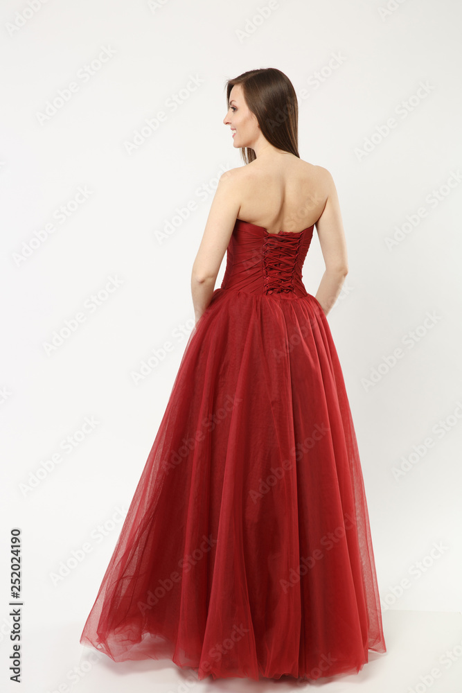 Full length photo of fashion model woman wearing elegant evening dress red gown posing isolated on white wall background studio portrait. Brunette long hair girl. Mock up copy space. Back rear view.