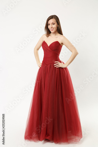 Full length photo of fashion model woman wearing elegant evening dress gown posing isolated on white wall background studio portrait. Brunette long hair girl. Mock up copy space. Red dress face view. © ViDi Studio