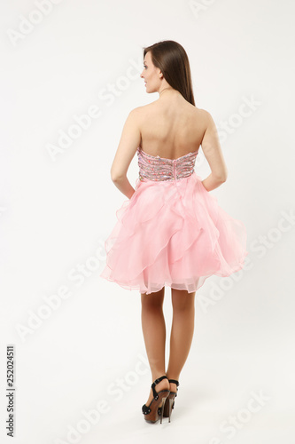 Full length photo of fashion model woman wearing elegant evening dress pink gown posing isolated on white wall background studio portrait. Brunette long hair girl. Mock up copy space. Back rear view.