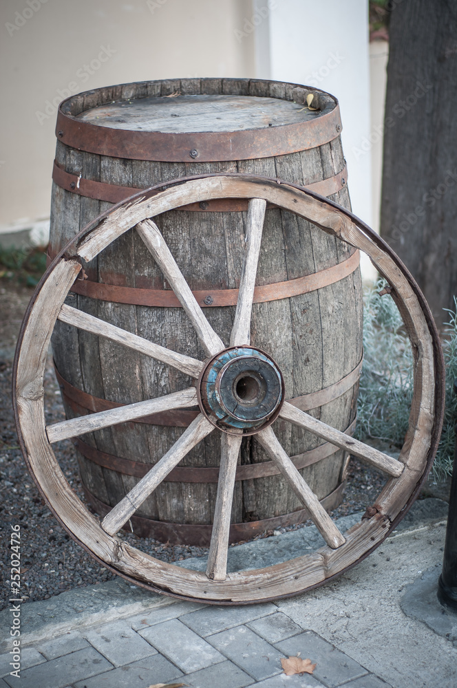 An old wooden cartwheel stands by a wooden barrel.