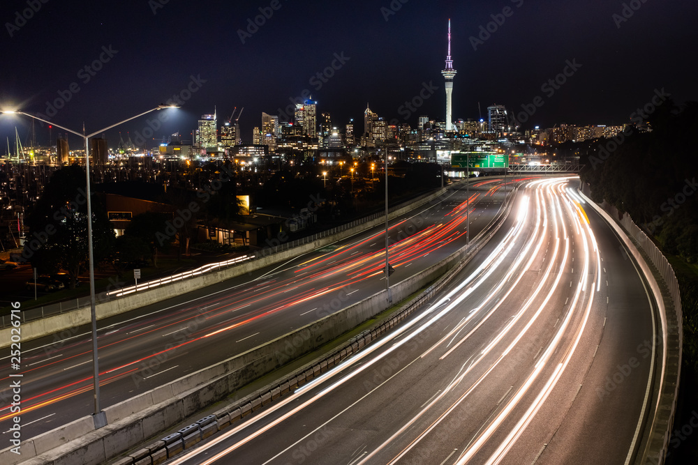 Car light trails at night heading into Auckland, with the city skyline