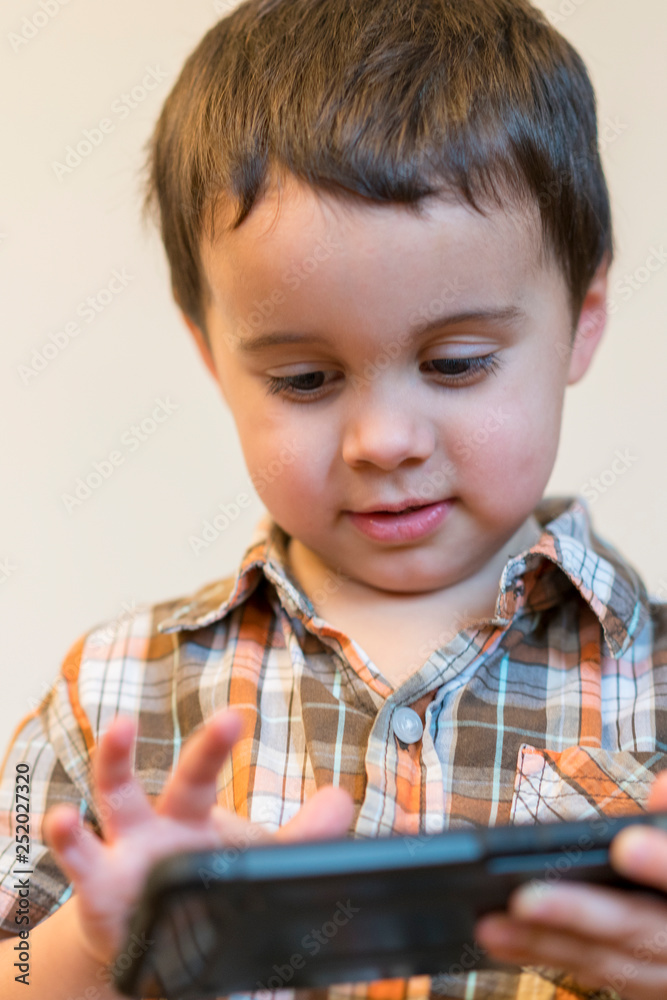 Portrait of a smiling little boy holding mobile phone isolated over light background. cute kid playing games on smartphone. vertical photo. close up Portrait of a smiling little boy holding mobile phone isolated over light background. cute kid playing games on smartphone. vertical photo. close up