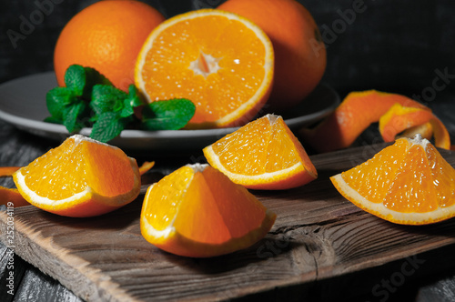 Juicy orange slices. In the background is a plate with orange fruits and mint. Wooden background. Photo taken in a dark style.