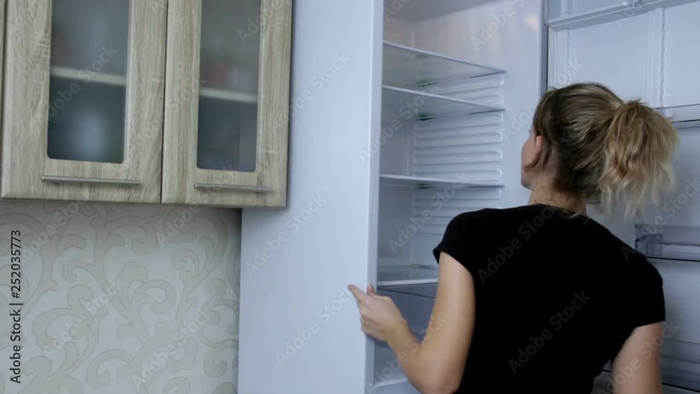 Woman opening the door of her empty fridge and looking inside