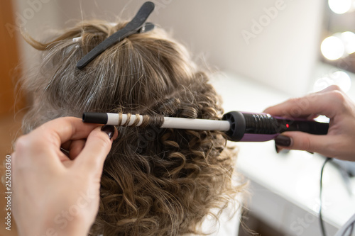 master doing curls, curl the hair with Curling iron, girl with blonde hair, close-up