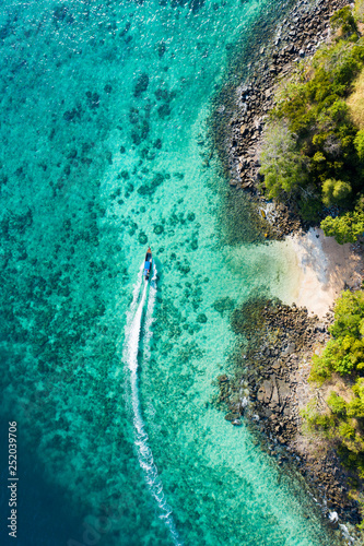 Fototapeta Naklejka Na Ścianę i Meble -  View from above, aerial view of a traditional long-tail boat sailing near a stunning barrier reef with a beautiful small beach bathed by a transparent and turquoise sea. Phi Phi Island, Thailand.