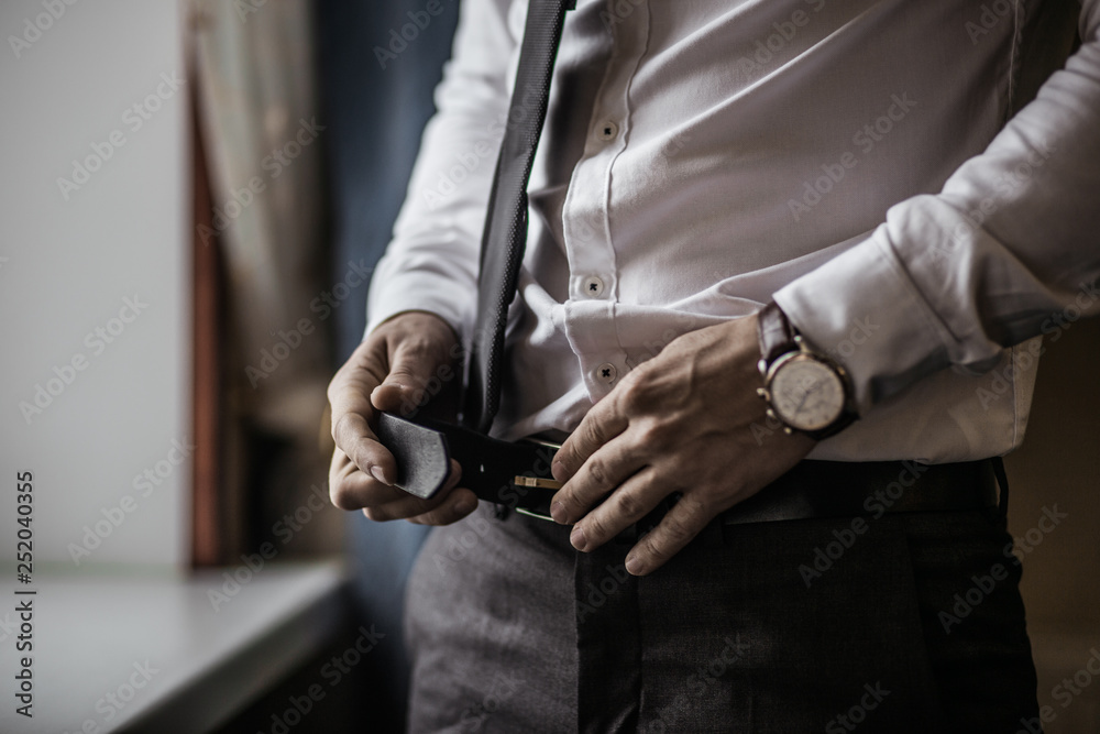 Groom in black tuxedo and bowtie correct his buttons on white shirt. Wedding. Details