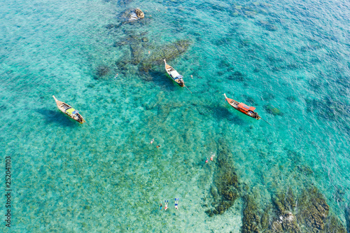 View from above, stunning aerial view of some long-tails boats and tourists who do snorkeling in a beautiful, transparent and turquoise sea, Phi Phi Island, Thailand.