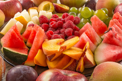 A mixture of their fruit. Peach, grapes, apple, watermelon, melon, raspberry, plum. Juicy and ripe pieces of fruit close-up.