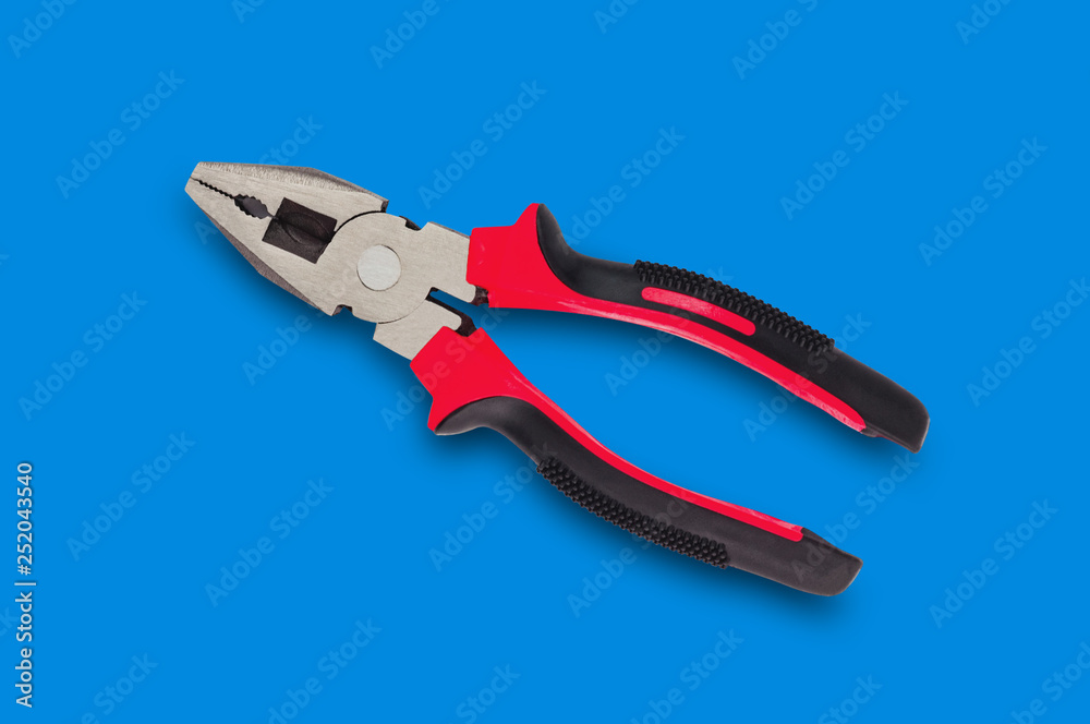 One new metal pliers with rubber handles black and red color in center on blue table. Top view. Repair or building concept One new metal pliers with rubber handles black and red color in center on blue table. Top view. Repair or building concept