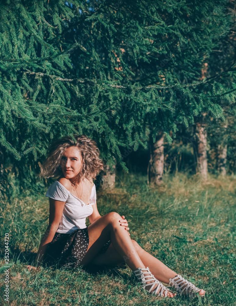 curly girl sitting in a relaxed pose under the tree in the summer and basking in the sun