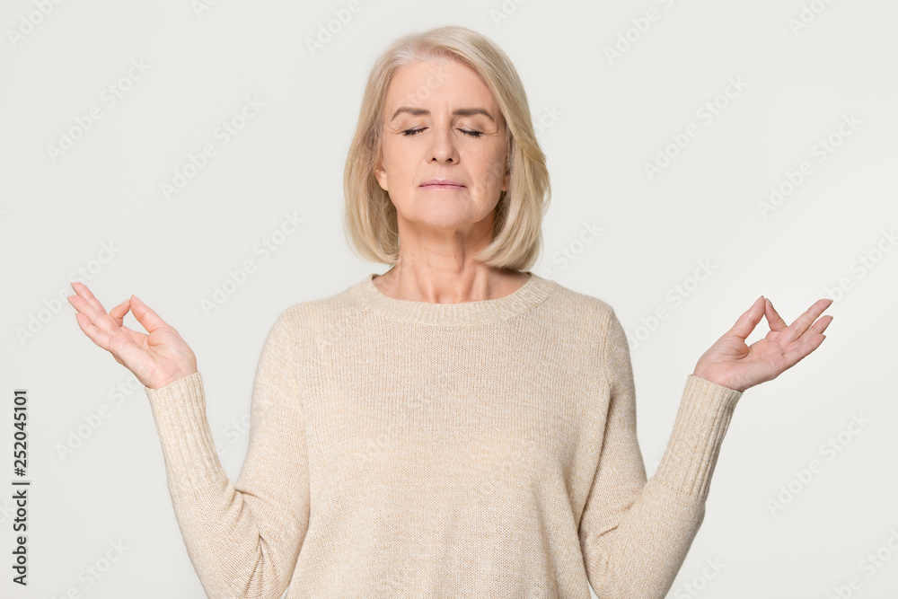 Calm healthy old woman meditating isolated on grey studio background Calm healthy old woman meditating isolated on grey studio background