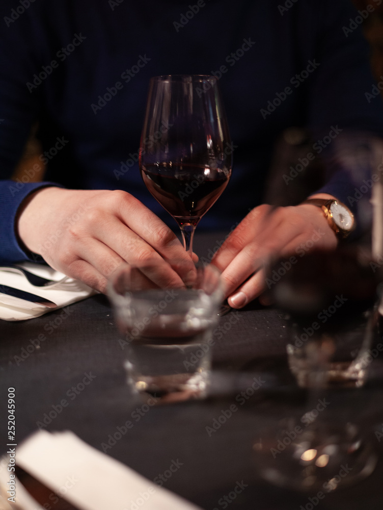hands of a man sitting at a table in a restaurant, in front of him is a glass of wine