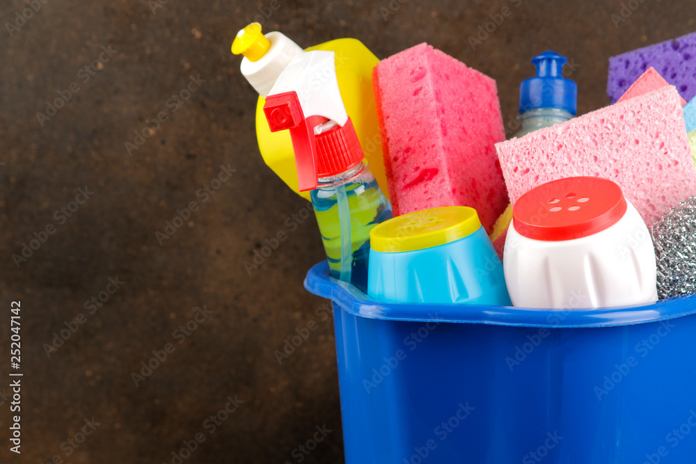 Bottles with cleansers and detergents in a blue bucket on a brown background. cleaning. cleaning products. close-up Bottles with cleansers and detergents in a blue bucket on a brown background. cleaning. cleaning products. close-up