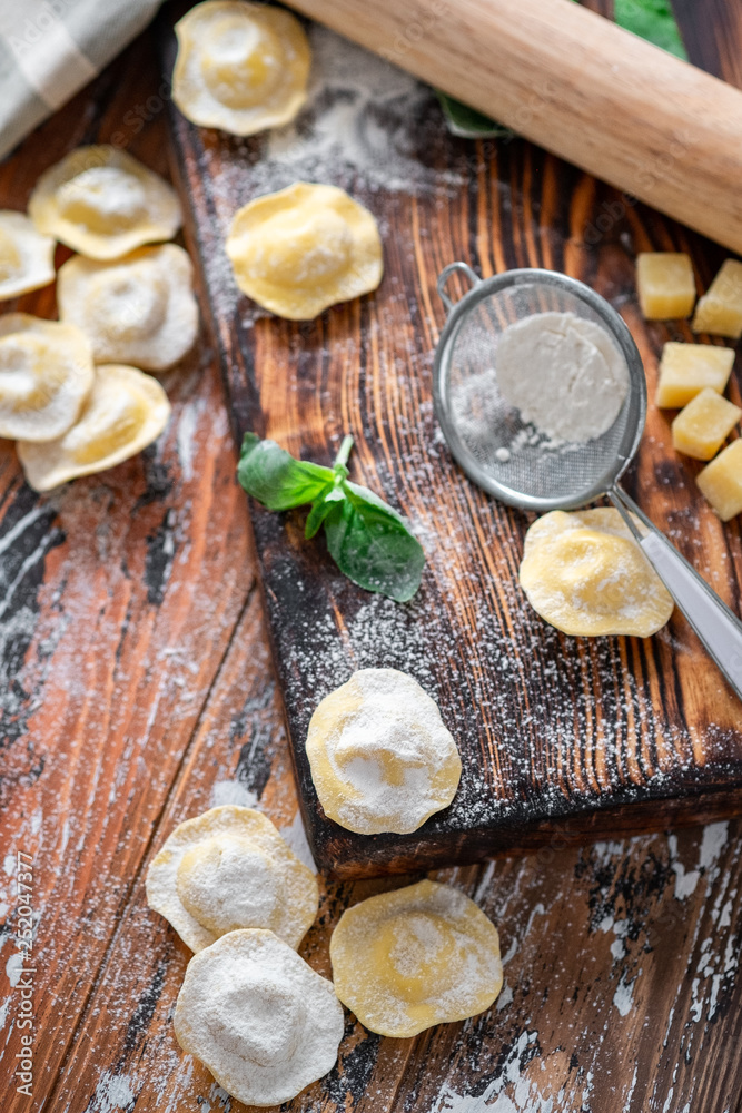 Raw Italian Ravioli pasta with Parmesan and Basil on a wooden background with flour, top view, recipe concept