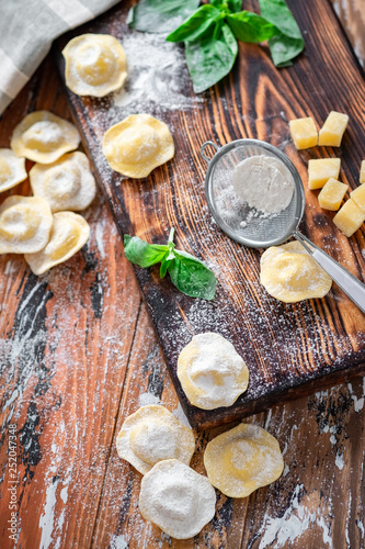 Raw Italian Ravioli pasta with Parmesan and Basil on a wooden background with flour, top view, recipe concept