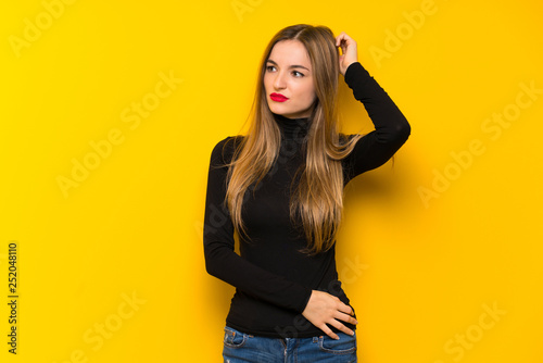 Young pretty woman over yellow background having doubts while scratching head
