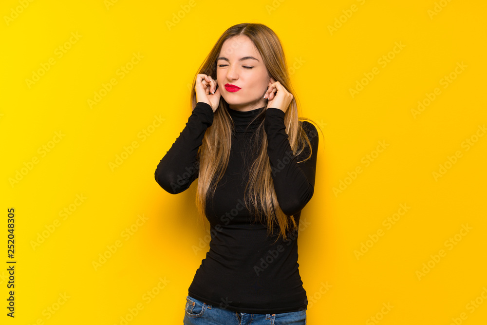 Young pretty woman over yellow background covering ears with hands. Frustrated expression Young pretty woman over yellow background covering ears with hands. Frustrated expression