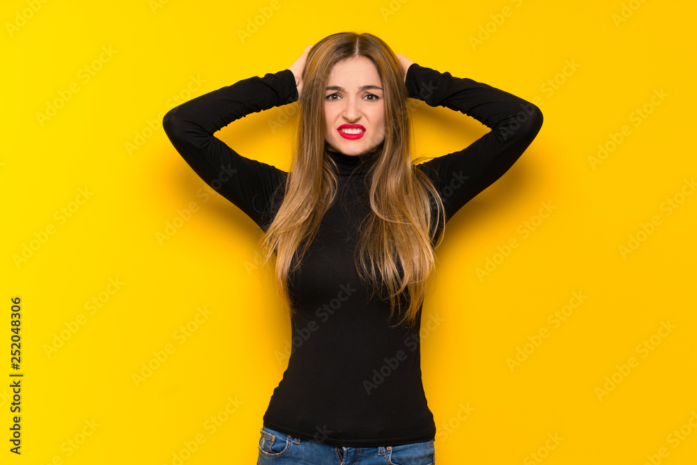 Young pretty woman over yellow background takes hands on head because has migraine