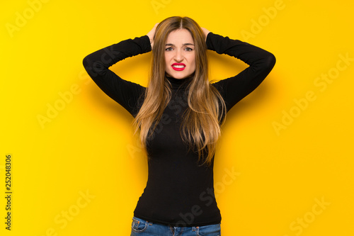 Young pretty woman over yellow background takes hands on head because has migraine