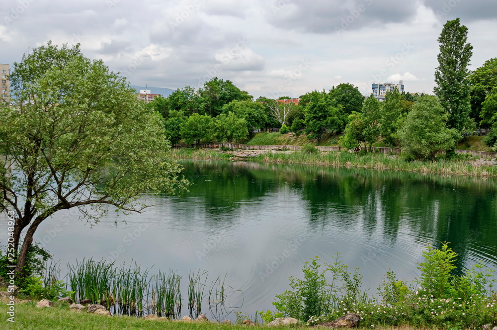 Spring panorama of a part of residential district neighborhood along a lake with green trees, shrubs and flowers, Drujba, Sofia, Bulgaria 