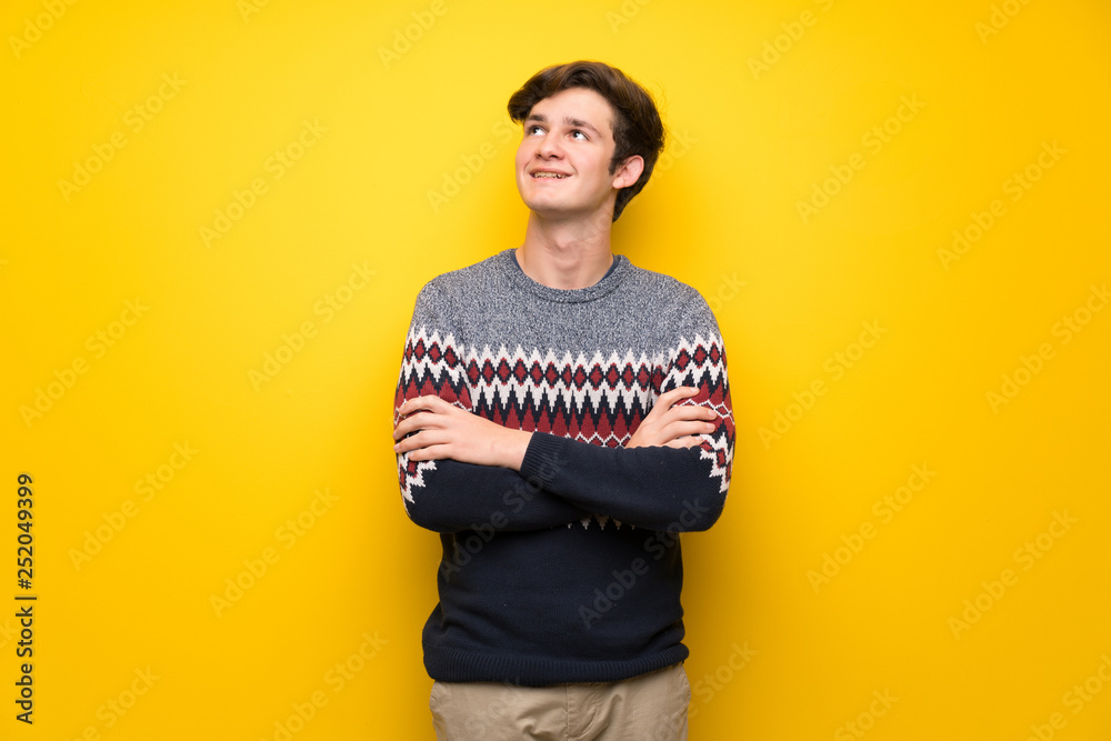 Fototapeta premium Teenager man over yellow wall looking up while smiling