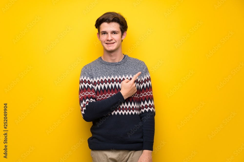Teenager man over yellow wall pointing to the side to present a product Teenager man over yellow wall pointing to the side to present a product
