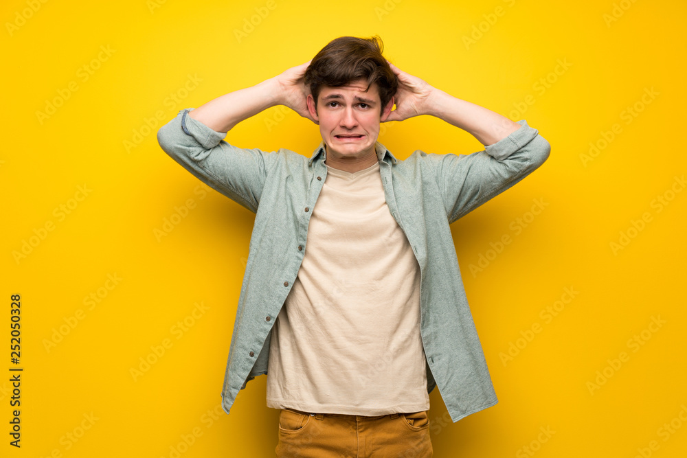 Teenager man over yellow wall takes hands on head because has migraine Teenager man over yellow wall takes hands on head because has migraine