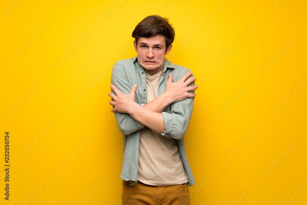 Teenager man over yellow wall freezing Teenager man over yellow wall freezing
