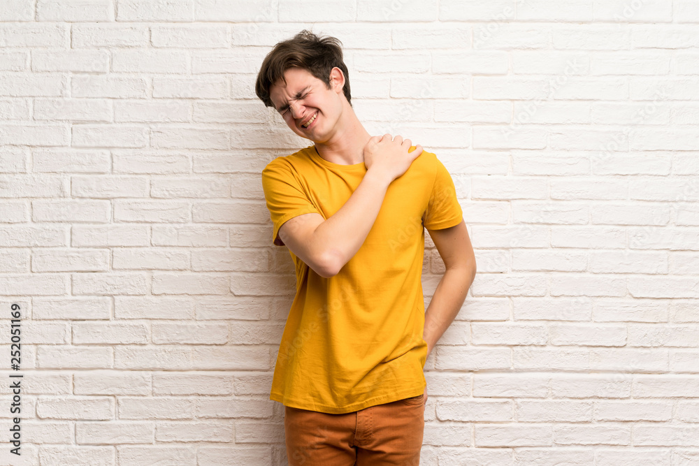Teenager man over white brick wall suffering from pain in shoulder for having made an effort Teenager man over white brick wall suffering from pain in shoulder for having made an effort