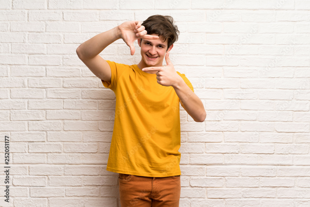 Teenager man over white brick wall focusing face. Framing symbol Teenager man over white brick wall focusing face. Framing symbol